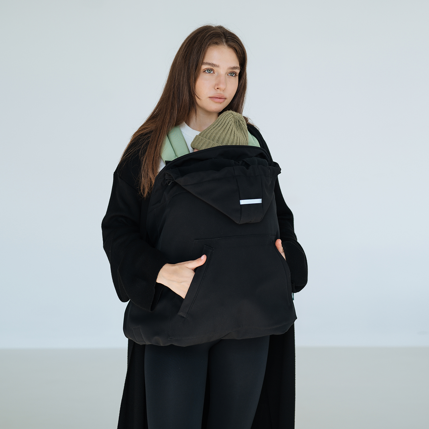 A mother wearing a black Love&Carry babywearing cover, keeping her baby warm during a walk.